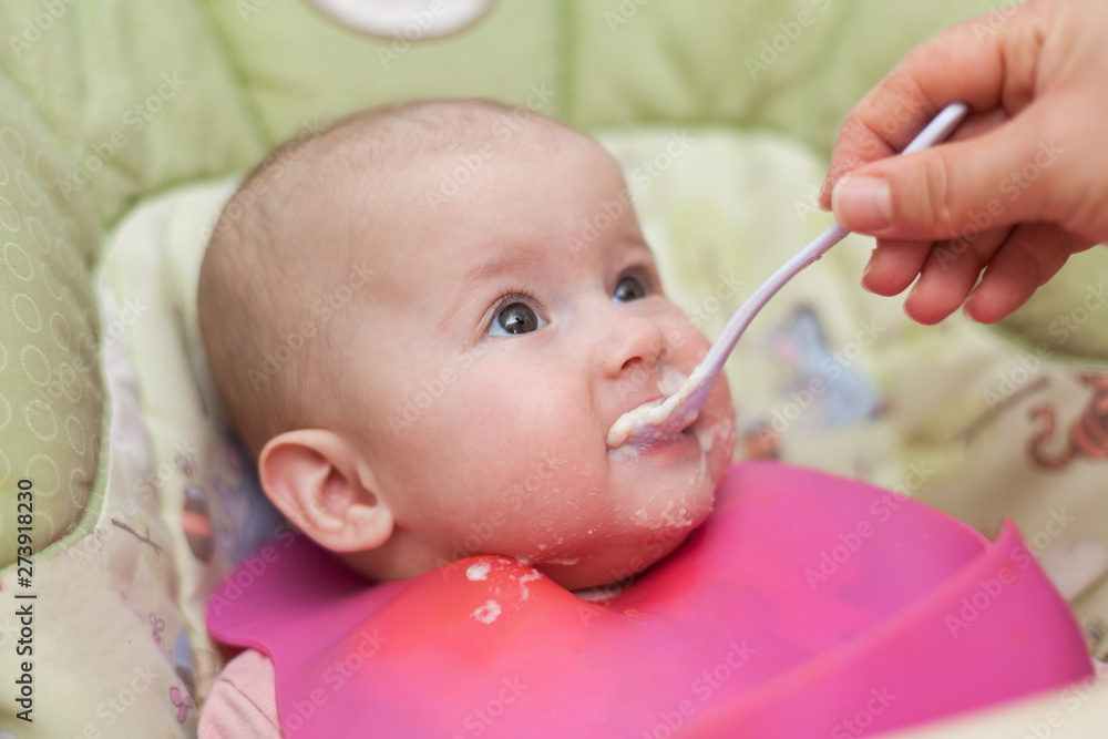 mother gives baby food from a baby spoon. baby eating food first time. weaning baby mother gives baby food from a baby spoon. baby eating food first time. weaning baby