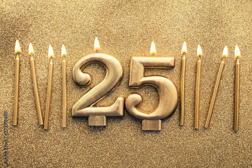 Number 25 gold celebration candle on a glitter background photo