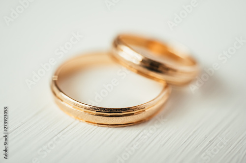 Close up of intersecting wedding gold rings on white wooden background. Side view.