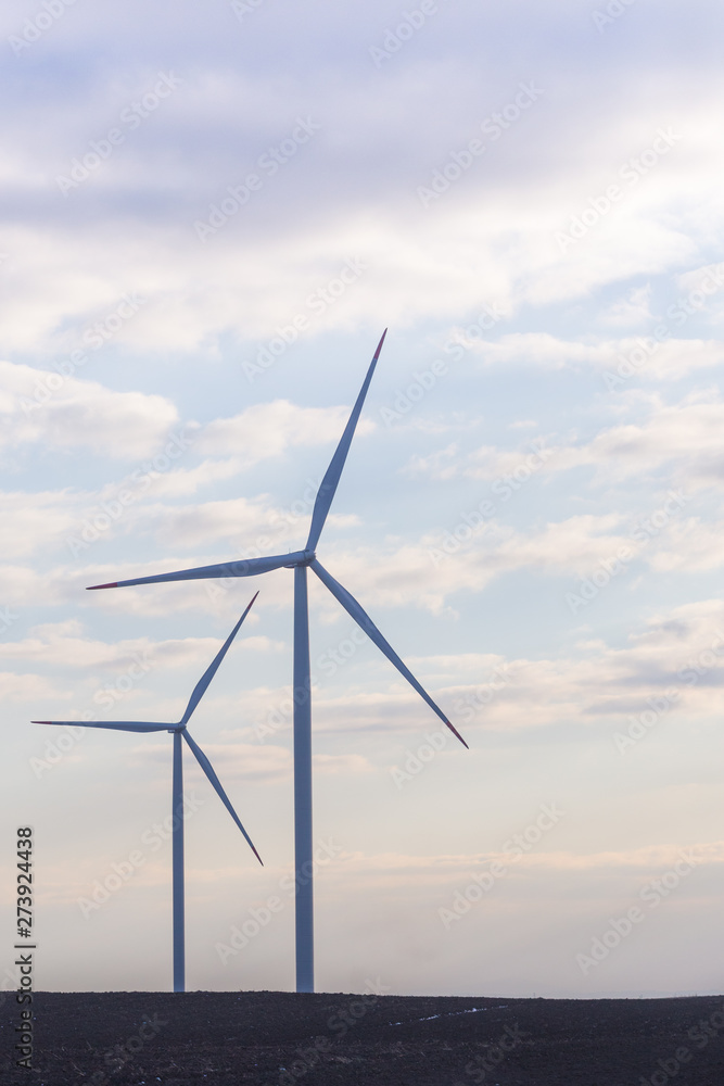 Two wind turbines on agricultural ground with cloudy sky in background
