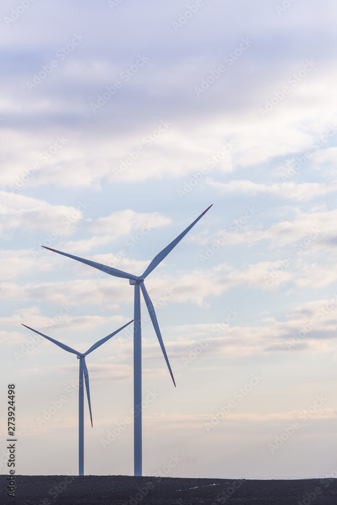 Two wind turbines on agricultural ground with cloudy sky in background Two wind turbines on agricultural ground with cloudy sky in background
