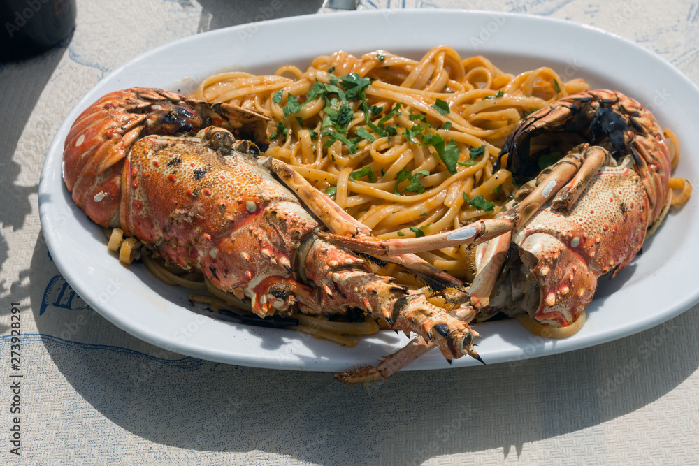 Delicious lunch by the sea. A white plate of spaghetti with huge lobsters on the grill. Travel to Santorini, Greece. Old port of Fira.