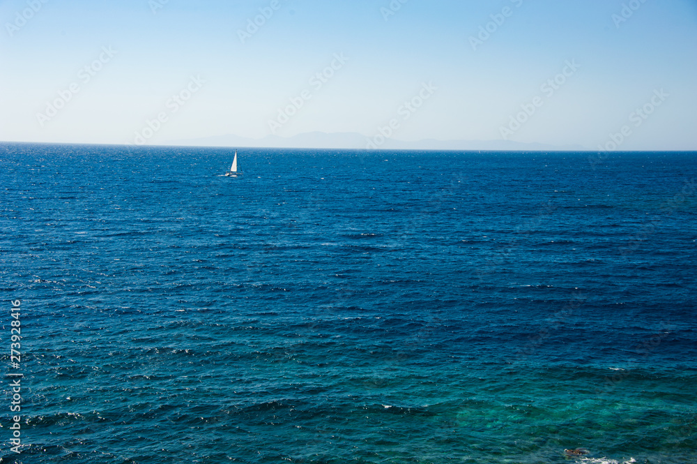 A lonely windsurfer, sailing in the endless blue ocean under the light blue sky of the Greek island Santorini / Thira 