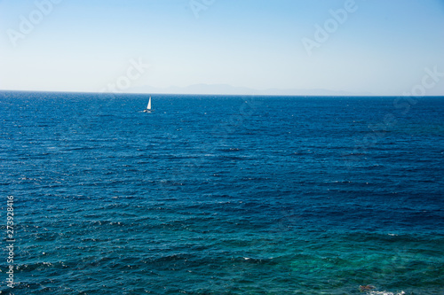 A lonely windsurfer, sailing in the endless blue ocean under the light blue sky of the Greek island Santorini / Thira 