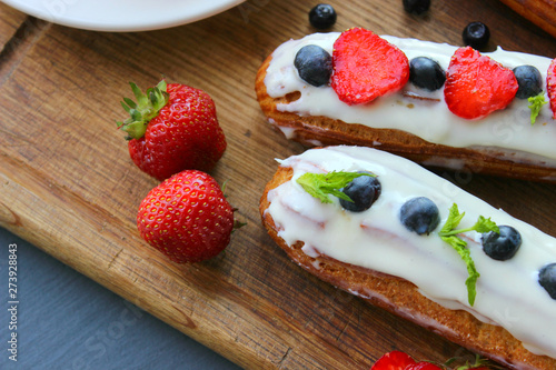 Delicious eclairs with strawberries and blueberries on a wooden cutting Board. Copy space. Beautiful and delicious dessert.