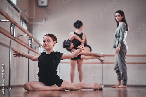 Little pretty girl is doing strechening while her other classmates doing exercises with teacher.