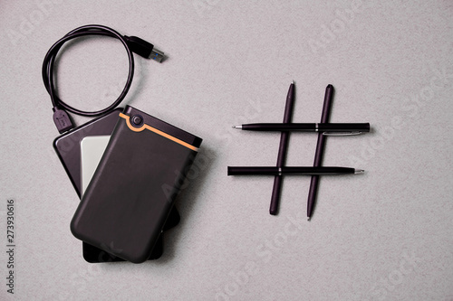 Gadget blogging, blog and blogger or social media concept: notepad, external hard drive and hashtag symbol on grey background. Flat lay