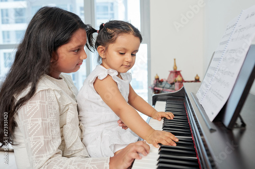 Older sister sitting together with her younger sister and teaching her to play the piano