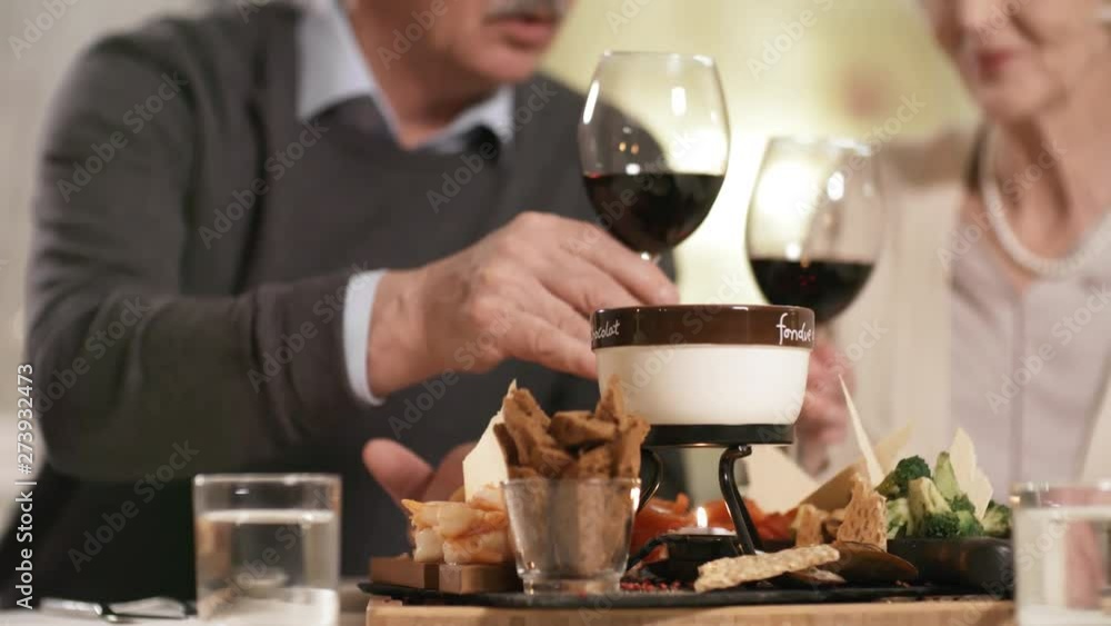 Panning close-up object shot of fondue platter with prawns, croutons and broccoli on table in restaurant, and senior couple sitting together over candlelit dinner and drinking red wine in background Panning close-up object shot of fondue platter with prawns, croutons and broccoli on table in restaurant, and senior couple sitting together over candlelit dinner and drinking red wine in background