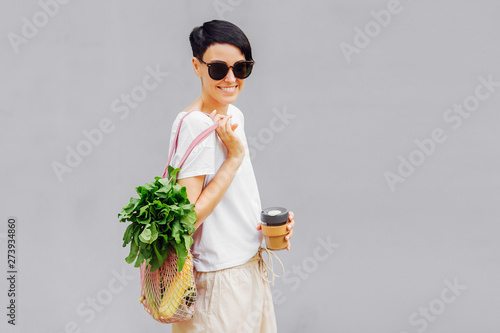 Young woman in light summer clothes with a eco bag of vegetables, greens and reusable coffee mug. Sustainable lifestyle. Eco friendly concept. photo