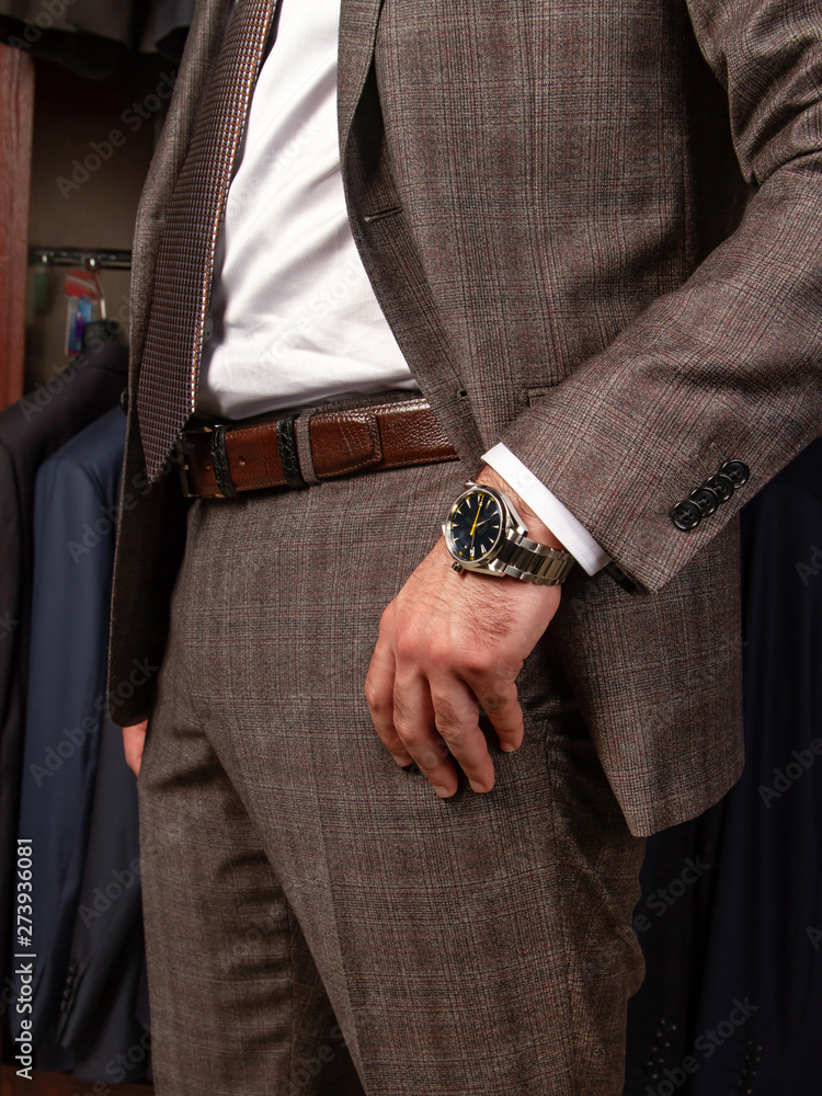 A man in a classic suit in a cage stands sideways, showing a wrist watch