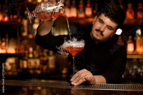 Bartender with strainer prepares an alcohol cocktail