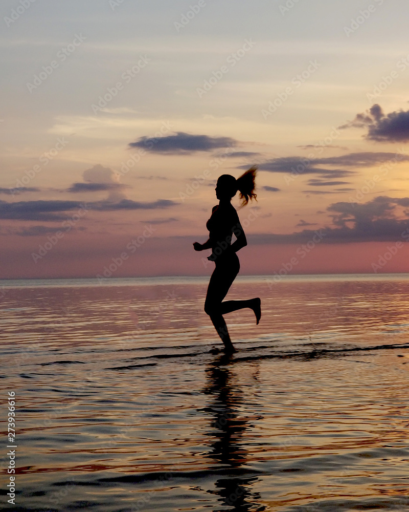 silhouette of a girl run on the beach sand. Shooting against the sun. Sunset over the sea