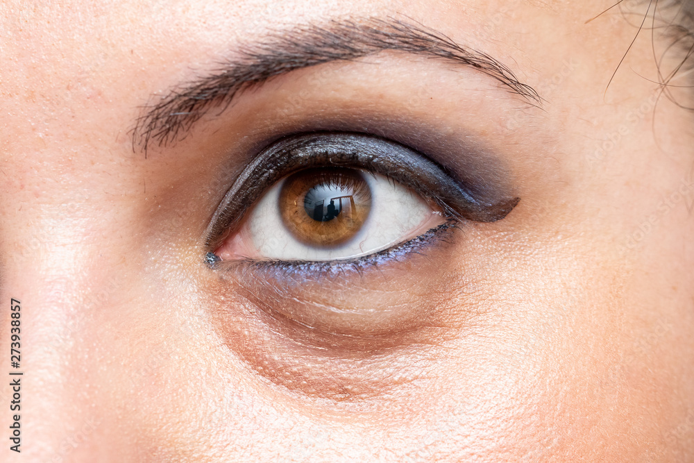 Obraz premium A macro view on the open eye of a young Caucasian woman, showing smoky blue eyeshadow with dark puffy circles beneath the eyes, caused by stress and tiredness.