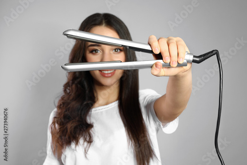 Happy woman with hair iron on grey background