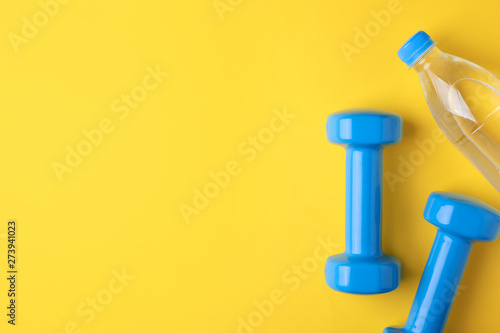 Vinyl dumbbells and bottle of water on color background, flat lay. Space for text