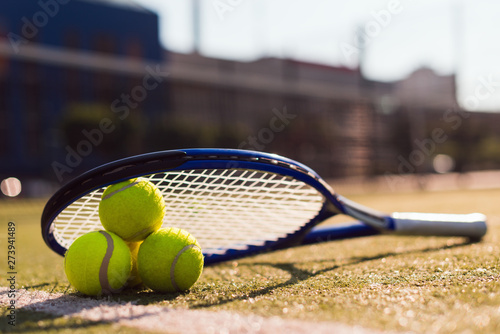 Three tennis balls and racket on hard court under sunlight © speed300