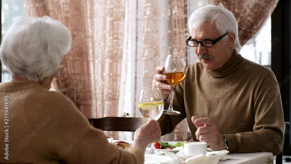 Medium shot of 60-something Caucasian gentleman, casually dressed in beige woolly jumper, eating healthy breakfast in hotel restaurant with his wife, drinking apple juice and lemon water, and chatting Medium shot of 60-something Caucasian gentleman, casually dressed in beige woolly jumper, eating healthy breakfast in hotel restaurant with his wife, drinking apple juice and lemon water, and chatting