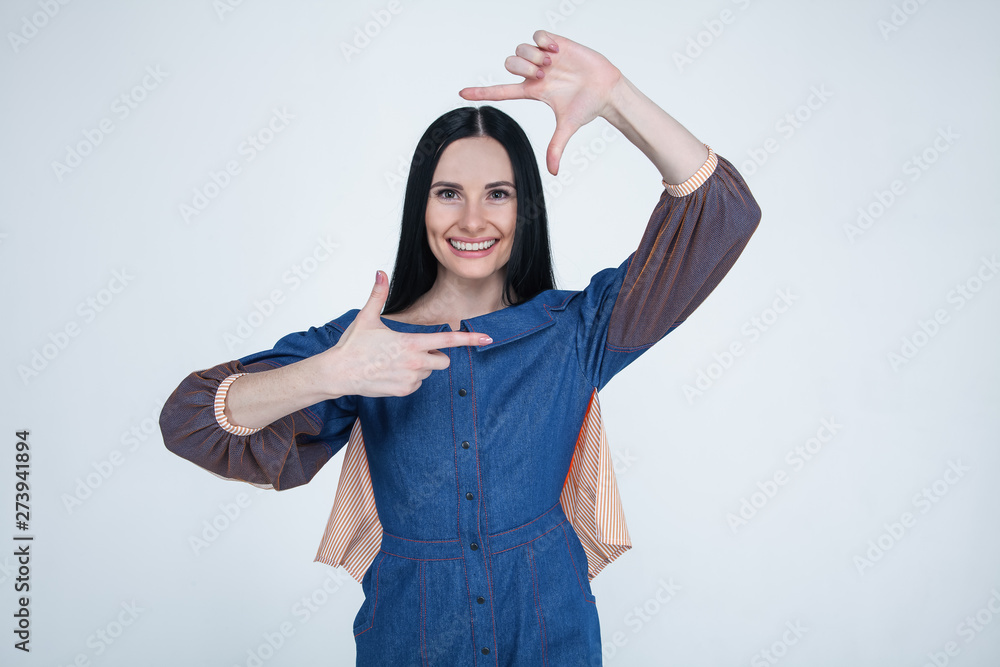 Portrait of young brunette positive female with cheerful expression, dressed in jeans dress, has good mood, gestures actively at camera. Beautiful dark-eyed woman posing indoors Portrait of young brunette positive female with cheerful expression, dressed in jeans dress, has good mood, gestures actively at camera. Beautiful dark-eyed woman posing indoors