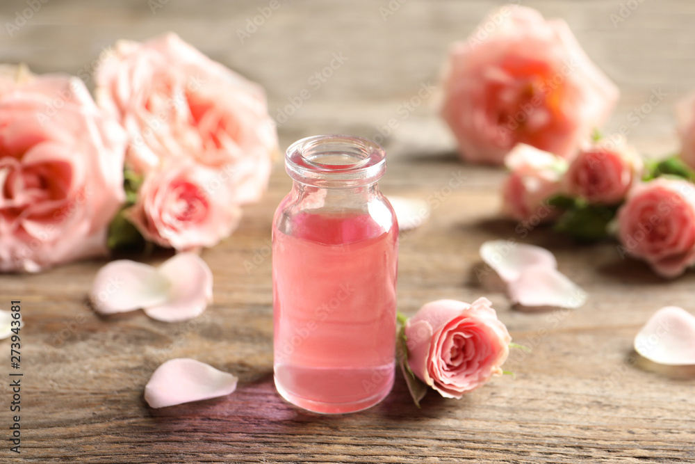 Bottle of rose essential oil and flowers on wooden table Bottle of rose essential oil and flowers on wooden table