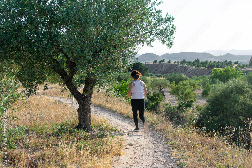 Fit middle-aged woman running through a rural field Fit middle-aged woman running through a rural field
