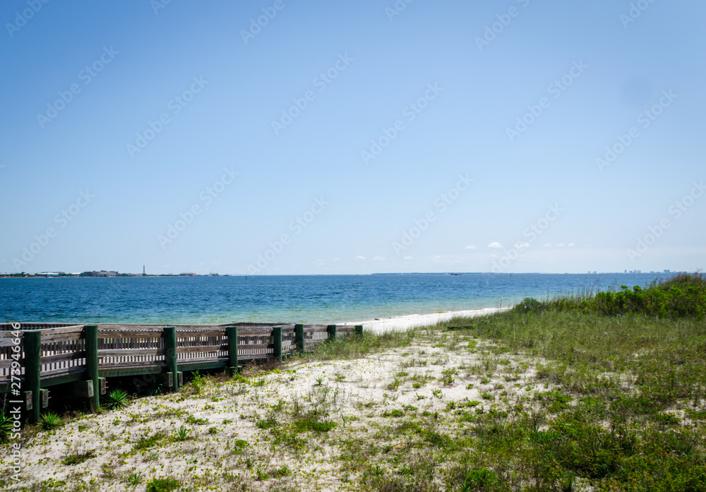  Ramp walkway leading to inter-coastal bay, ocean beach shoreline with waves splashing onshore. Pensacola, FL, USA in the background.