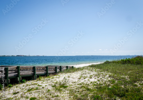  Ramp walkway leading to inter-coastal bay, ocean beach shoreline with waves splashing onshore. Pensacola, FL, USA in the background. © hildeanna