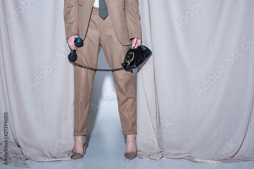 cropped view of model standing on light grey curtain background and phone handset in hand