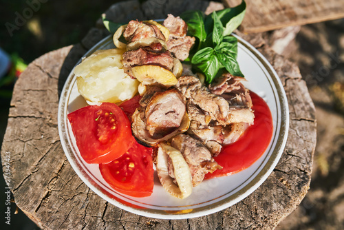 Pork kebab with boiled potatoes sliced tomato and Basil leaves on the white plate.  Selective focus. Poor country holiday food concept.