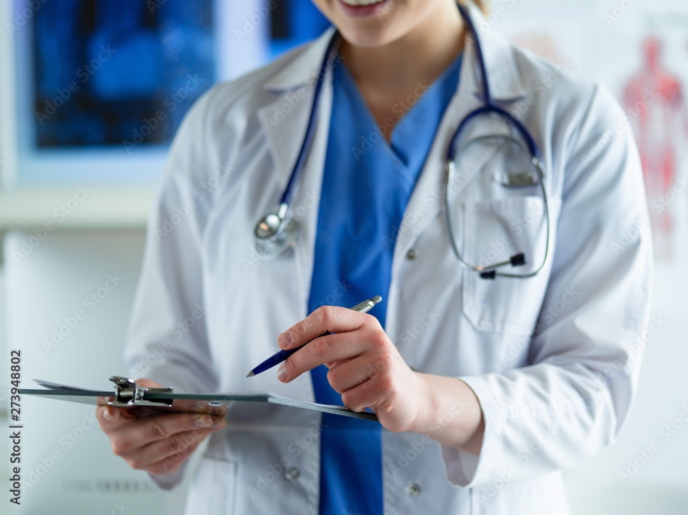 Doctor with a stethoscope, holding a notebook in his hand. Close-up of a female doctor filling up medical form at clipboard while standing straight in hospital Doctor with a stethoscope, holding a notebook in his hand. Close-up of a female doctor filling up medical form at clipboard while standing straight in hospital