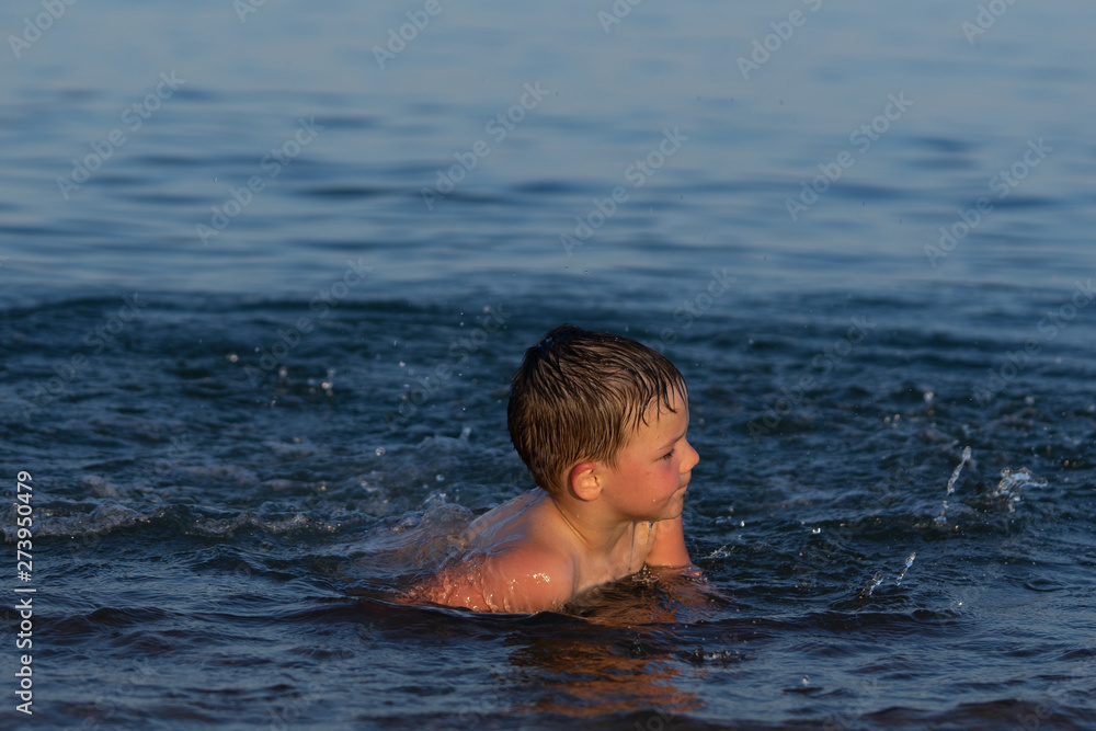 A boy of three years is swimming in the sea at sunset with his brother.
