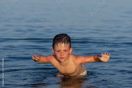 A boy of three years is swimming in the sea at sunset with his brother.