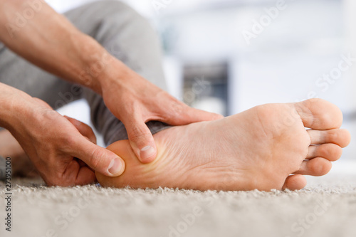 Man hands giving foot massage to yourself after a long walk, suffering from pain in heel spur, close up, indoors. Flat feet, leg fatigue, plantar fasciitis photo