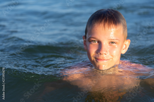 A boy of nine is swimming in the sea at sunset.