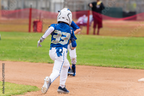 Youth baseball player in blue uniform and white helmet sprints across infield to steal second base.