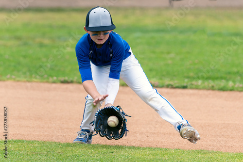 Принти на полотні Youth baseball player in blue uniform fielding a ground ball into his glove in the infield during a game