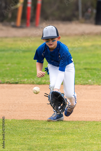 Youth baseball player in blue uniform keeping eyes on a ground ball into his glove in the infield during a game.