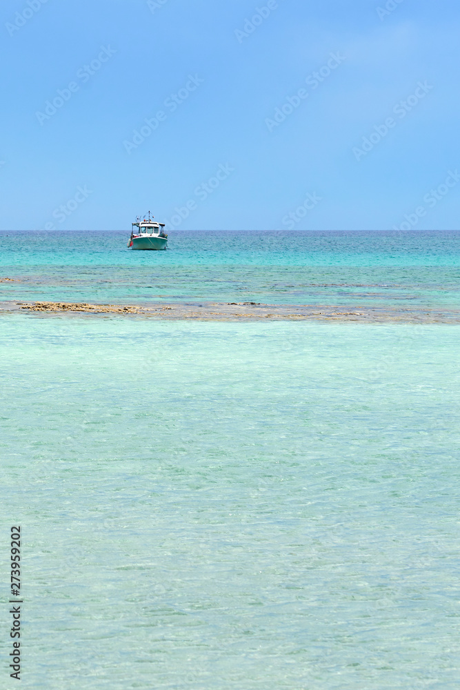 Turquoise blue sea water on a lagoon with a ship on a horizon line ander a cloudy sky. Copy space.