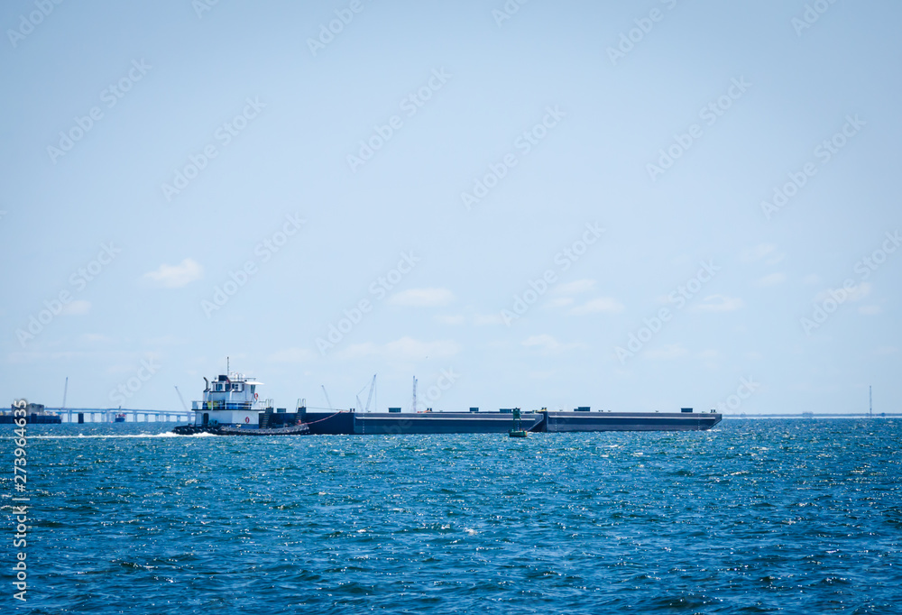Barge being pushed by a tugboat in tropical blue ocean water. Freight industry using waterway shipping lanes.