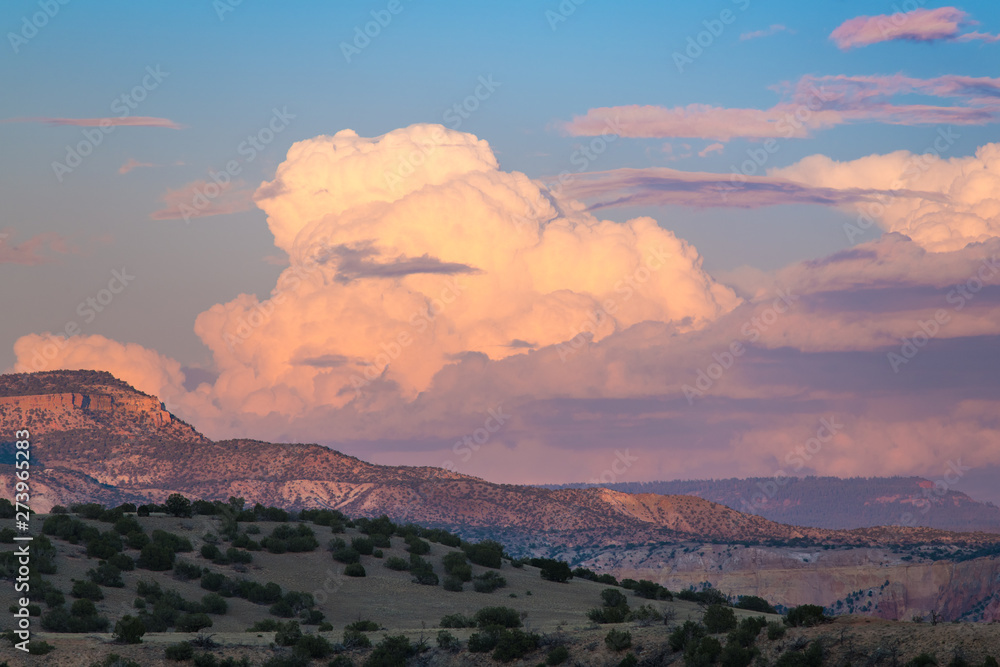 Fototapeta premium Sunset paints cumulus clouds and thunderheads in soft colors of pink, purple and peach over the colorful desert landscape of Ghost Ranch, Abiquiu, New Mexico