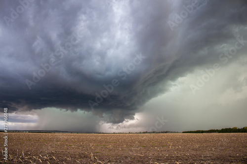 A supercell thunderstorm dumps heavy rain and hail over an empty field.