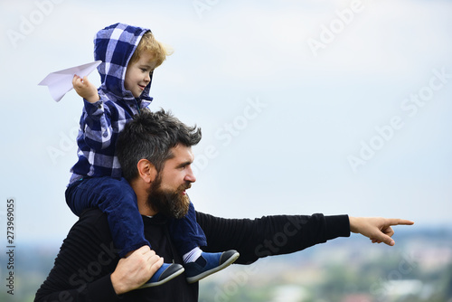 Father giving son ride on back in park. Father and son building together a paper airplane. Happy child playing with toy paper plane against summer sky background.