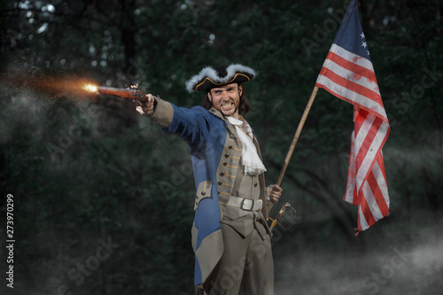 Billede på lærred Epic Portrait of man dressed as soldier of american revolution war of United States aims from pistol with flag