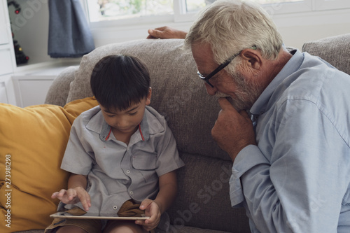 senior man happiness and grandson are sitting on the sofa and playing games and using tablet at living room together