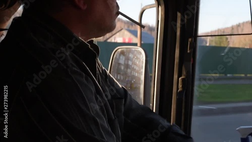 The driver in the cabin of the bus goes on the route smokes while dThe driver behind the wheel of the bus in the rays of the sun reflected from the side mirror, while the bus is moving along the road  photo