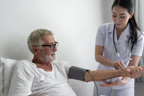 senior man with smiling nurse, takes care and discussion after health check by stethoscope and cheer on bed at nursing home