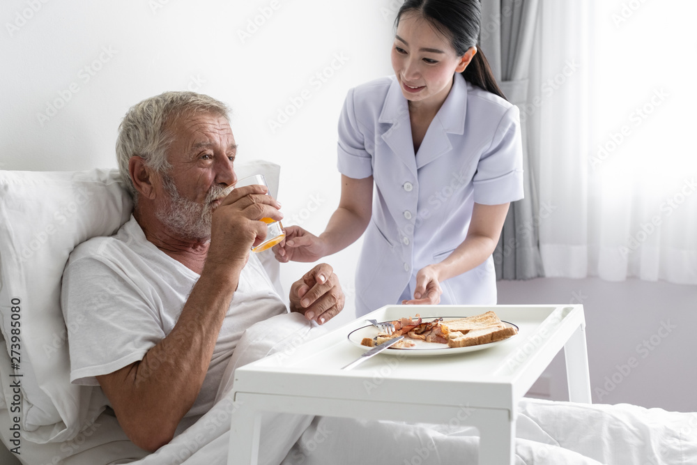 senior man with smiling nurse, takes care breakfast and discussion and cheer on bed at nursing home senior man with smiling nurse, takes care breakfast and discussion and cheer on bed at nursing home