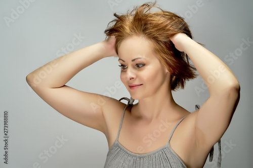 Beautiful attractive red-haired woman poses in studio on gray background.