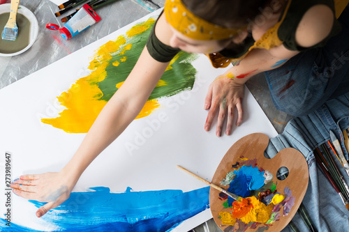 Finger painting hobby. Top view of female artist sitting on floor, using blue and yellow colors to create abstract artwork. photo