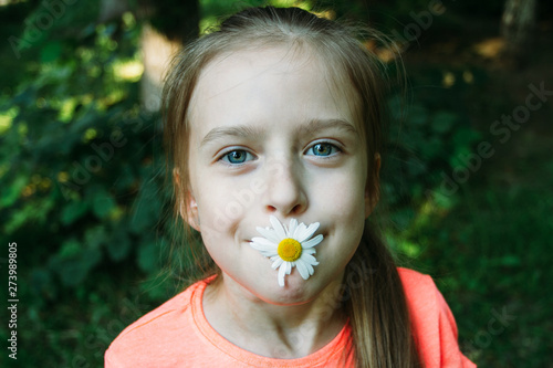 Funny  smiling little girl with camomile flower in her mouth. Summer mood.